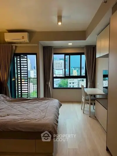 Modern bedroom with city view, featuring a cozy bed and study area, perfect for urban living.