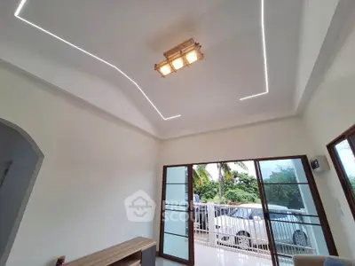 Modern living room with stylish ceiling lights and large windows opening to a balcony with garden view.
