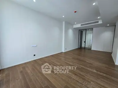 Spacious empty room with wooden flooring and modern glass door, perfect for customization.
