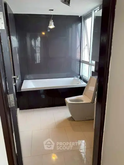 Modern bathroom with sleek black tiles and large bathtub, featuring natural light from large windows.