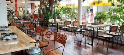 Spacious restaurant interior with wooden tables, chairs, and lush greenery, perfect for dining and relaxation.