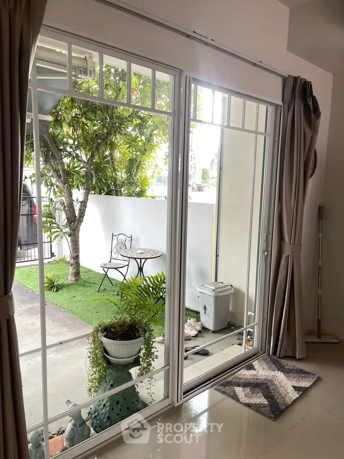 Charming patio view through sliding glass doors with lush greenery and cozy seating area.