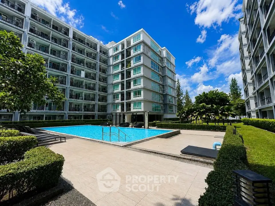 Modern apartment complex with pool and lush greenery under a clear blue sky.