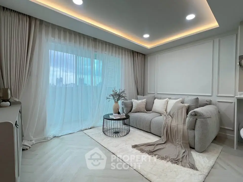 Elegant living room with cozy gray sofa, chic decor, and large window with sheer curtains.