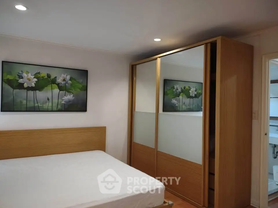 Cozy bedroom with wooden wardrobe and floral artwork, perfect for relaxation.