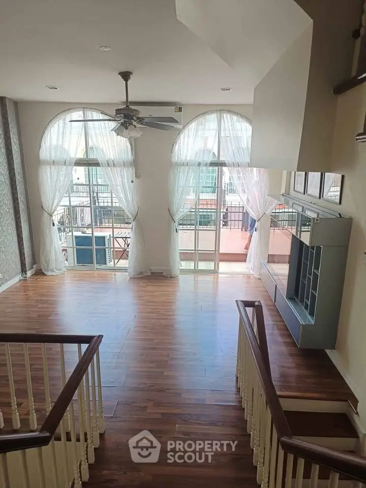 Spacious living room with elegant wooden flooring and large windows opening to a balcony.