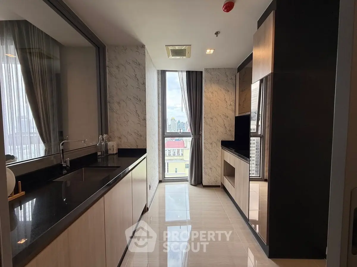 Modern kitchen with sleek black countertops and city view, featuring a closed layout and ample natural light.