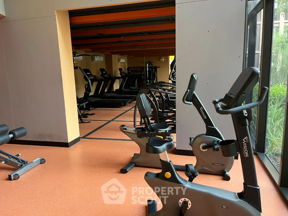 Spacious gym with modern exercise equipment and large windows for natural light.