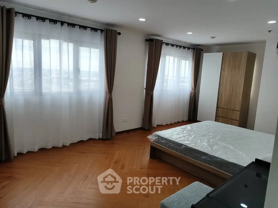 Spacious bedroom with large windows and wooden flooring in modern apartment.