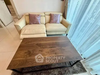 Modern living room with beige sofa and wooden coffee table near large window with sheer curtains.