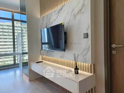 Modern living room with sleek TV setup and marble accent wall, offering a glimpse of city view.