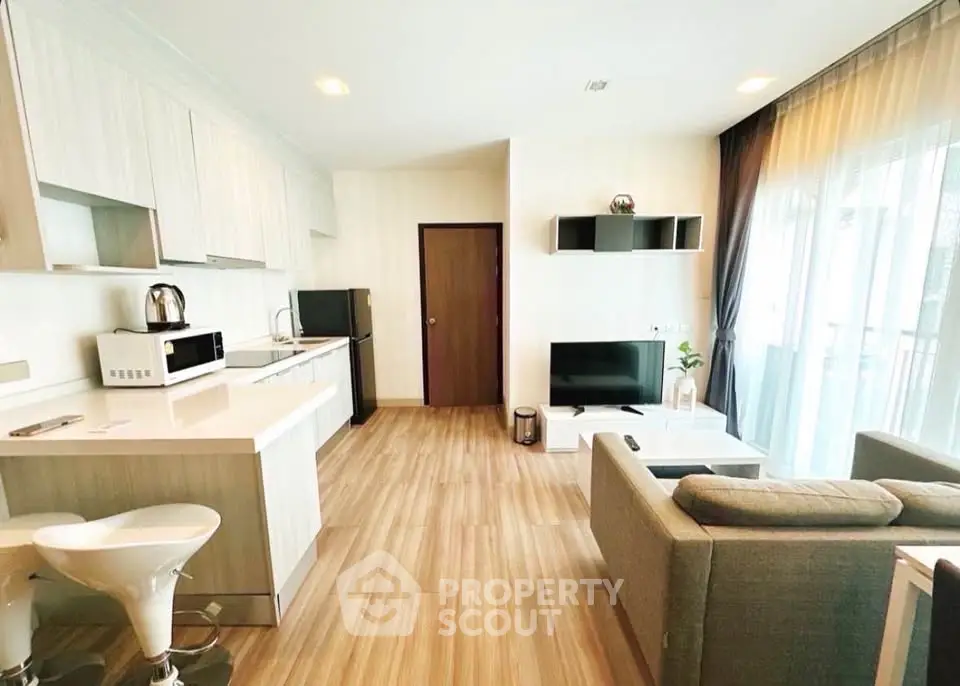 Modern open-layout living room with kitchen, featuring sleek furniture and natural light.