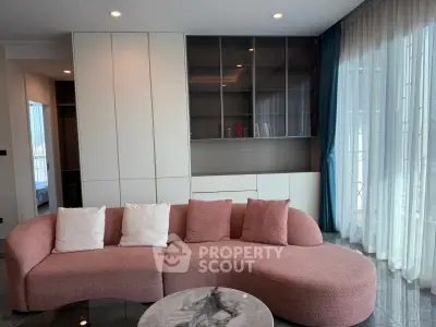 Modern living room with stylish pink sofa and elegant shelving unit, featuring floor-to-ceiling windows.