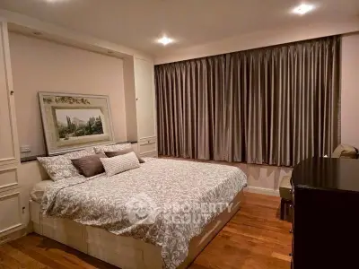 Elegant bedroom with cozy bedding and stylish decor, featuring hardwood floors and large window with curtains.