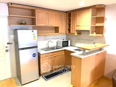 Modern kitchen with wooden cabinets, stainless steel fridge, and microwave in cozy apartment.