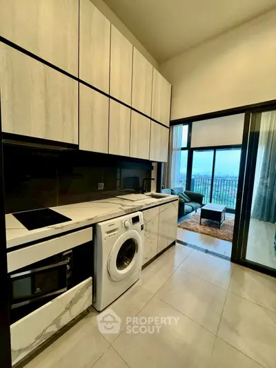 Modern kitchen with washing machine and open layout to living room with balcony view.