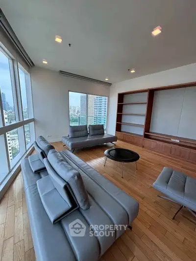 Spacious modern living room with city view, featuring sleek gray sofas and wooden flooring.