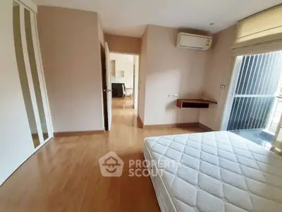 Spacious bedroom with wooden flooring and natural light, featuring a large window and air conditioning.