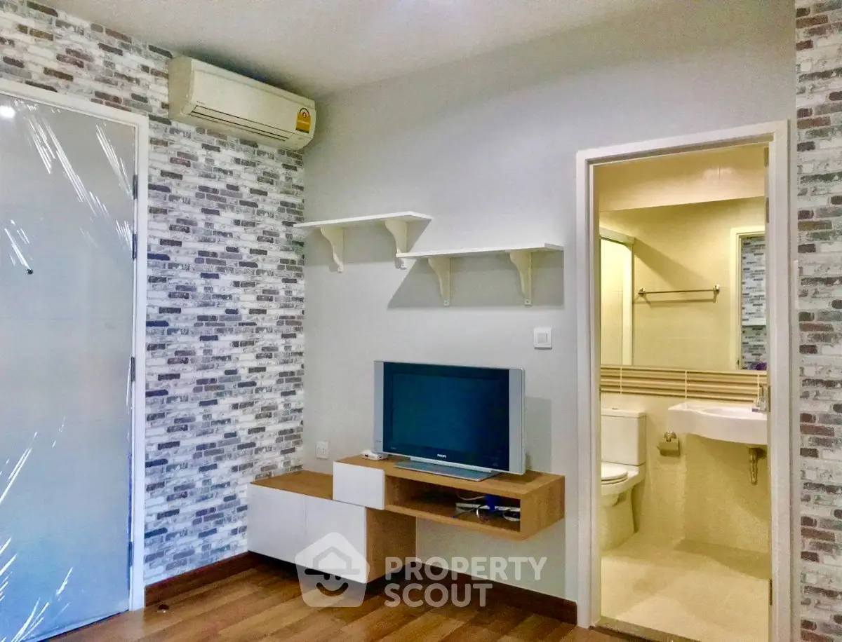 Modern living room with TV and bathroom view, featuring stylish brick accent wall and wooden flooring.