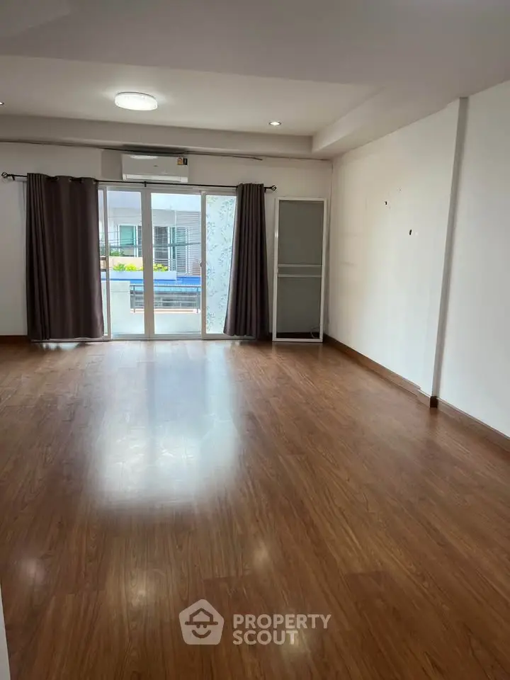 Spacious empty living room with wooden flooring and large windows leading to a balcony.