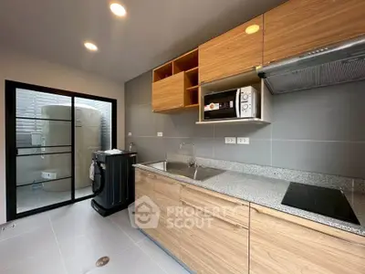 Modern kitchen with sleek cabinets and appliances, featuring a washing machine and microwave.