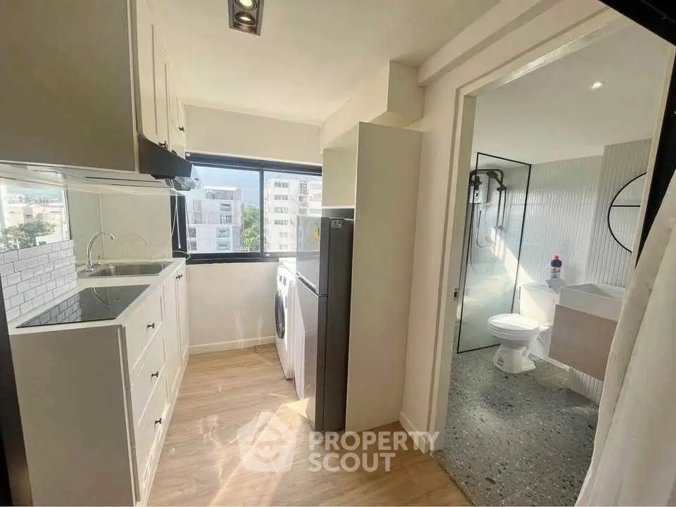 Modern apartment kitchen with open layout and adjacent bathroom, featuring sleek appliances and natural light.