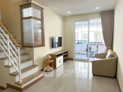 Modern living room with staircase and large window, featuring sleek furniture and natural light.