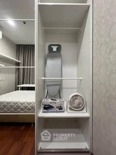 Spacious bedroom closet with ironing board and fan, perfect for organized living.