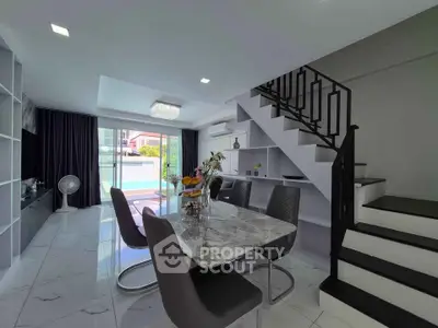 Modern dining area with marble table and staircase in stylish open-plan living space.