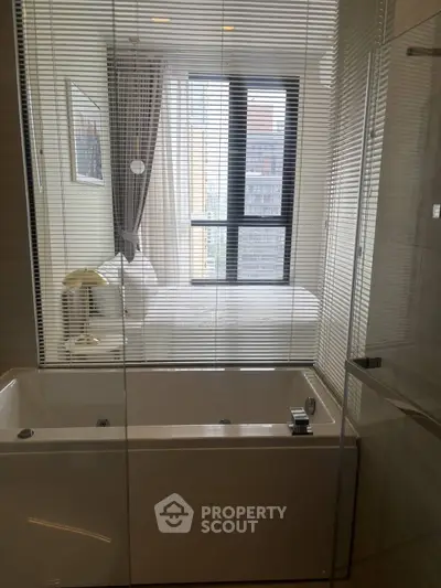 Modern bathroom with bathtub and view into a stylish bedroom through glass partition.