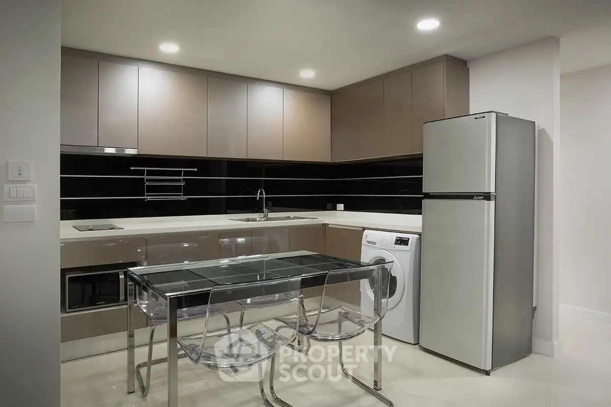 Modern kitchen with sleek cabinetry, glass dining table, and integrated appliances in a stylish apartment.