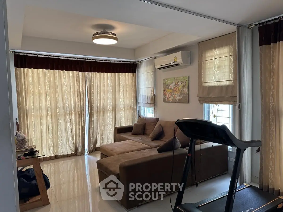Spacious living room with modern sofa and treadmill, featuring large windows and elegant curtains.