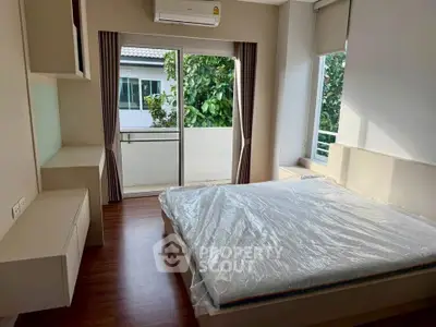 Bright bedroom with large window and balcony access, featuring modern furnishings and air conditioning.