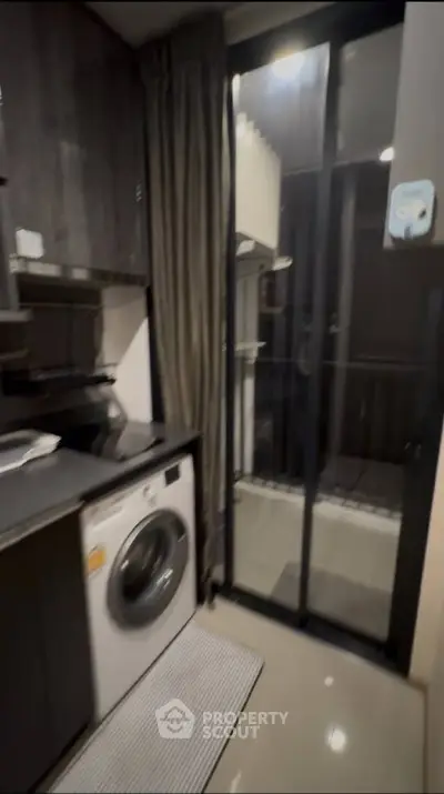 Modern kitchen with washing machine and balcony access in sleek apartment.