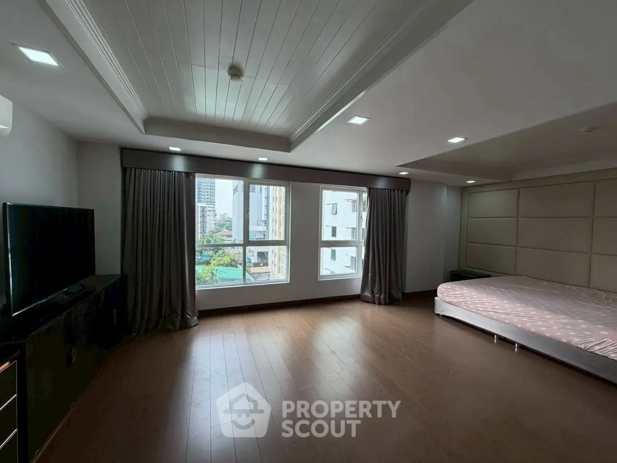 Spacious bedroom with large windows and wooden flooring in modern apartment