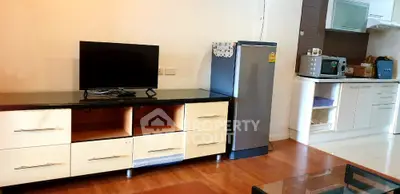 Modern living room with TV, fridge, and kitchen appliances in open layout.
