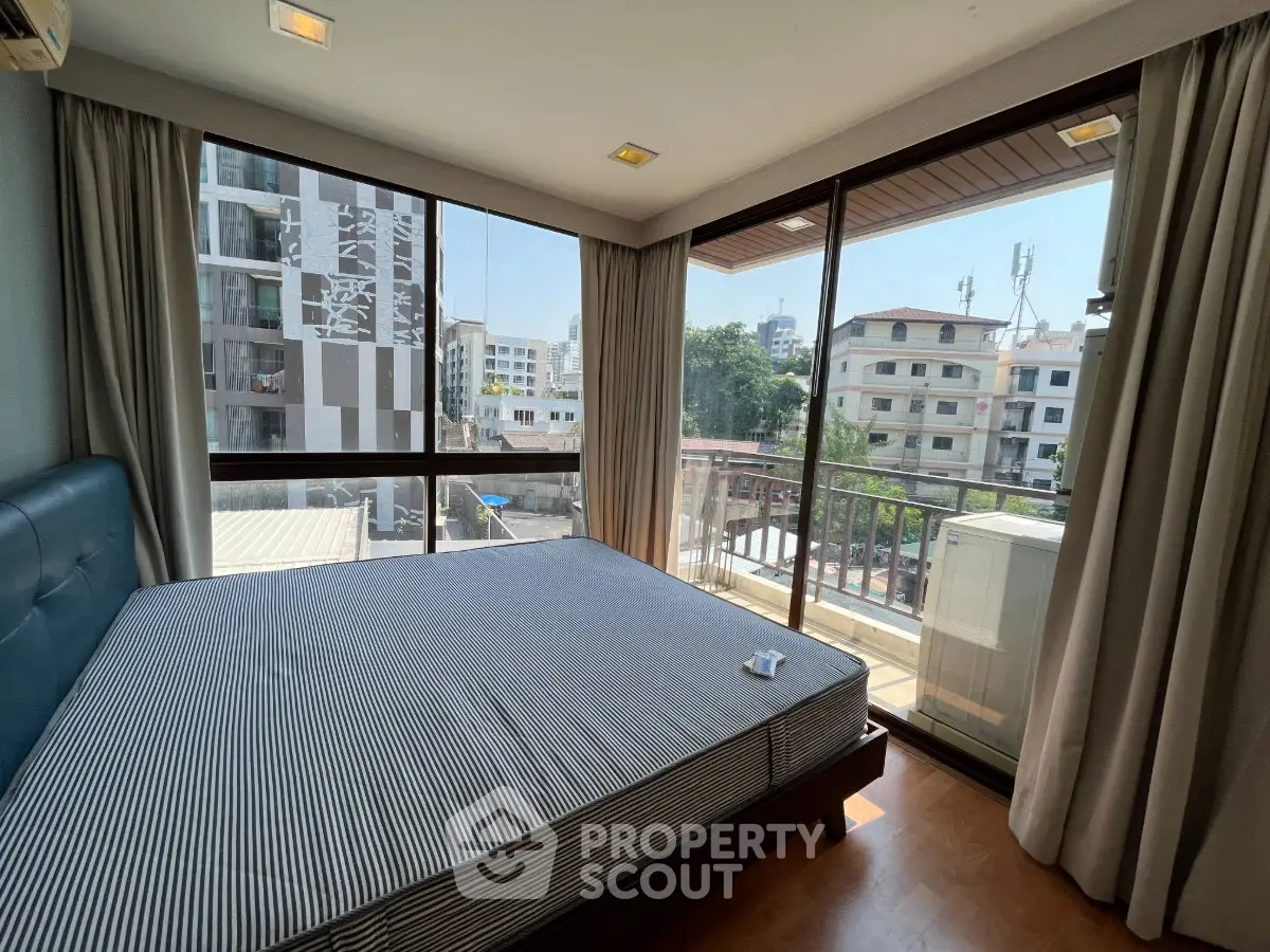 Spacious bedroom with large windows offering city views in modern apartment.