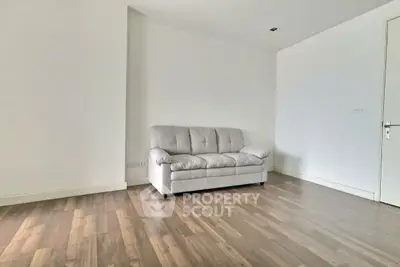 Spacious minimalist living room with wooden flooring and a cozy sofa, perfect for modern living.