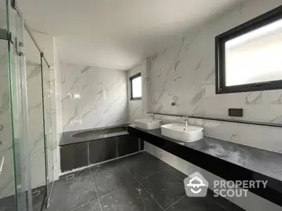 Elegant bathroom with marble walls, sleek design, and modern fixtures, featuring a spacious glass shower and dual vessel sinks.