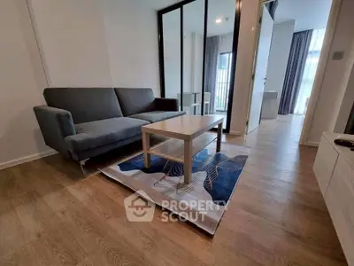 Modern living room with sleek gray sofa and wooden flooring, featuring a stylish rug and mirrored wardrobe.