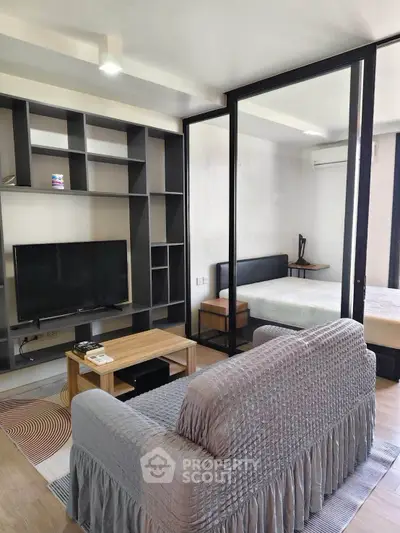 Modern living room with glass partition leading to a cozy bedroom, featuring stylish shelving and a comfortable sofa.