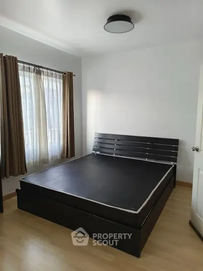 Spacious bedroom with modern bed frame and natural light through large window.