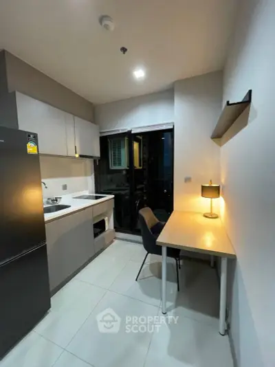 Modern kitchen with sleek design and integrated workspace, featuring a fridge and ample storage.