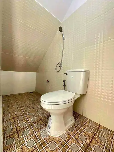 Unique bathroom with sloped ceiling and retro tile flooring, featuring a modern toilet and shower setup.