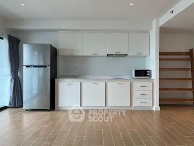 Modern kitchen with sleek white cabinets, stainless steel fridge, and microwave in open layout.