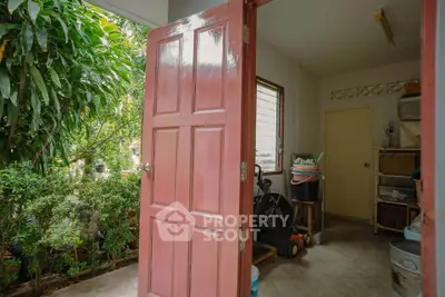 Charming garden view from a cozy utility room with open door and lush greenery.