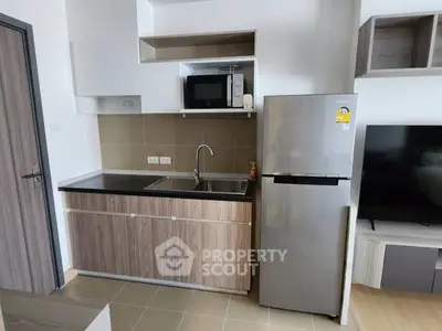 Modern kitchen with sleek cabinetry, stainless steel fridge, and built-in microwave in a compact apartment.