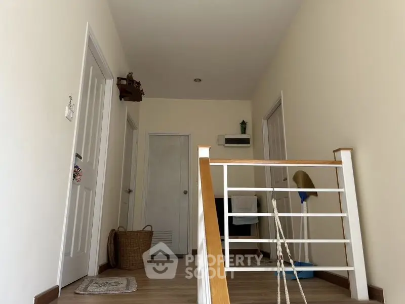 Bright hallway with wooden flooring and white doors, featuring a modern railing.