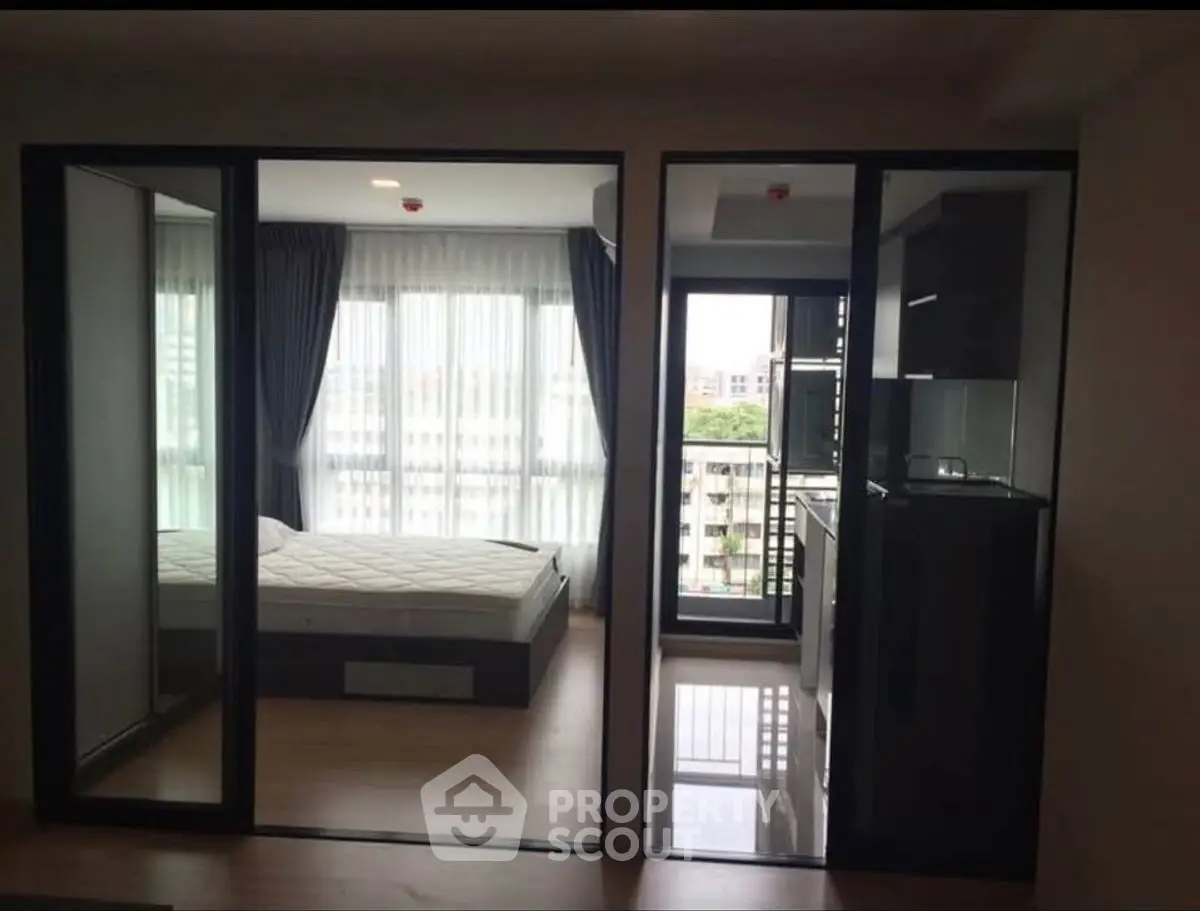 Modern apartment with glass partitions, featuring a bedroom and compact kitchen area.