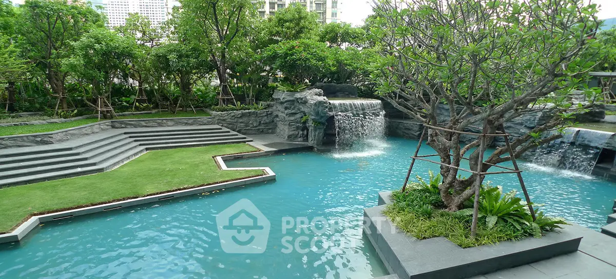 Luxurious outdoor pool with waterfall and lush greenery in modern residential complex.